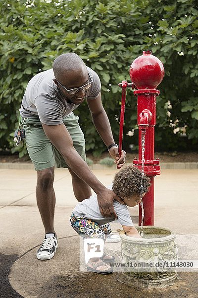 Vater und kleiner Sohn benutzen Wasserbrunnen im Park