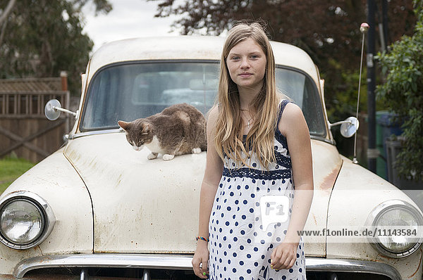 Girl standing near cat on vintage car