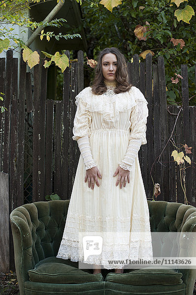 Kaukasische Frau in altem Kleid auf dem Sofa stehend