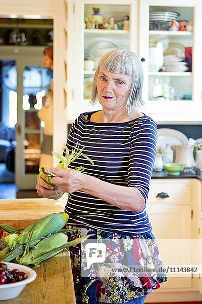 Ältere kaukasische Frau  die in der Küche Mais schält