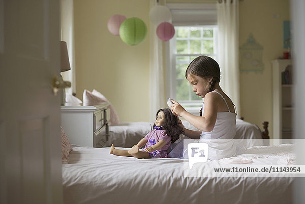 Kaukasisches Mädchen bürstet die Haare einer Puppe auf dem Bett