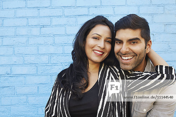 Indisches Paar  das sich entlang einer blauen Backsteinmauer umarmt