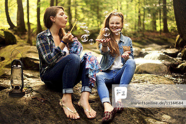 Girls blowing bubbles on forest rock