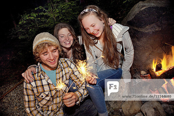 Friends playing with sparklers near campfire