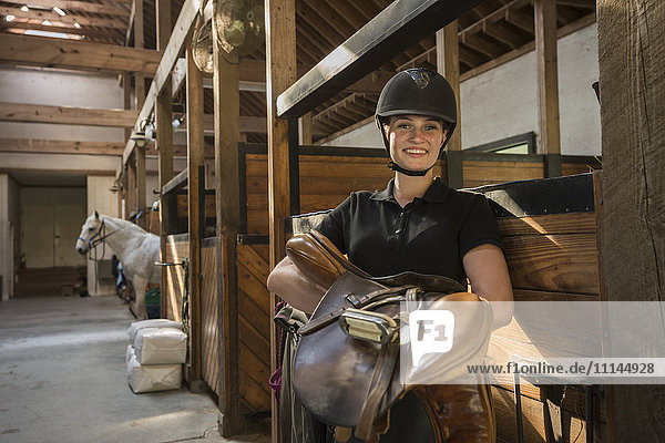 Kaukasisches Mädchen trägt Sattel im Pferdestall