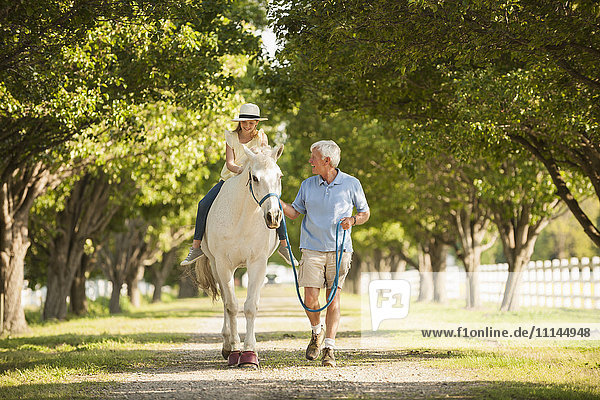 Kaukasischer Mann,  der mit seiner Enkelin auf einem Pferd spazieren geht