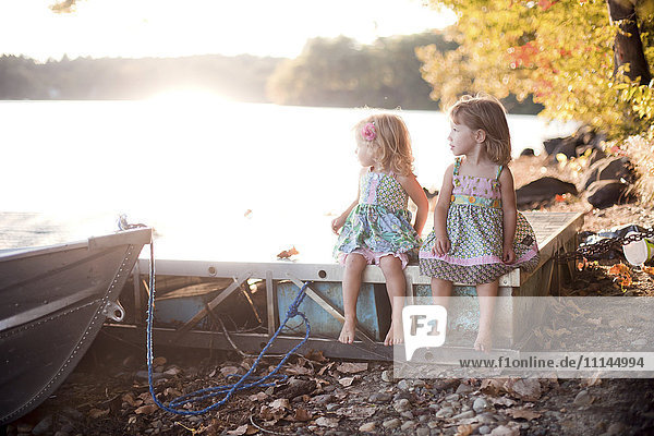 Mädchen sitzen auf einem Holzsteg an einem ländlichen See