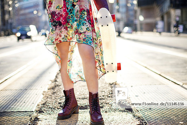 Woman carrying skateboard on city sidewalk