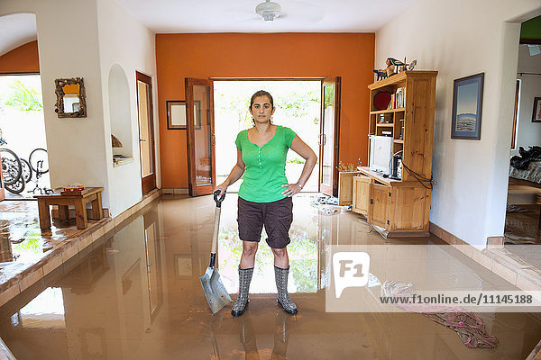 Hispanische Frau schaufelt Wasser aus einem überfluteten Haus