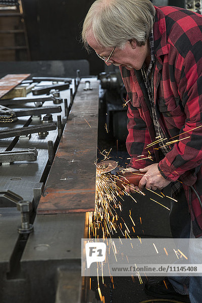 Caucasian man sanding metal in metal shop