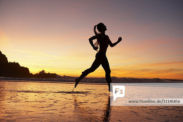 Silhouette of woman running on beach at sunset