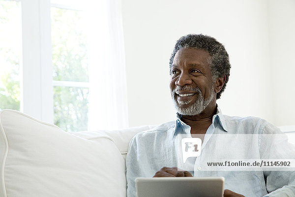 Älterer Mann mit digitalem Tablet auf dem Sofa