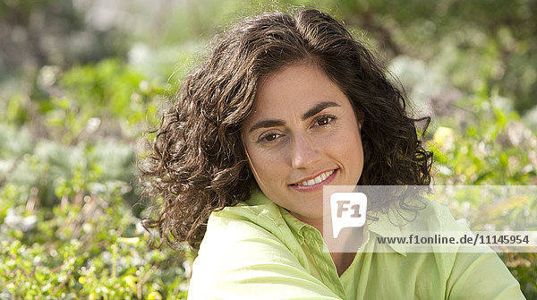 Lächelnde hispanische Frau sitzt im Garten