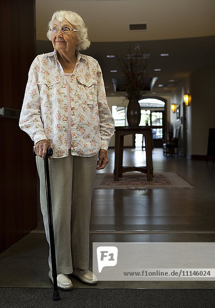 Ältere kaukasische Frau mit Stock im Altersheim stehend