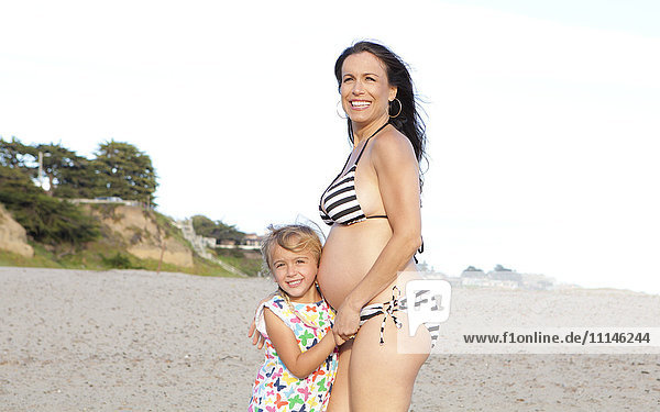 Pregnant Caucasian mother and daughter standing on beach