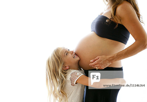 Kaukasisches Mädchen umarmt schwangere Mutter