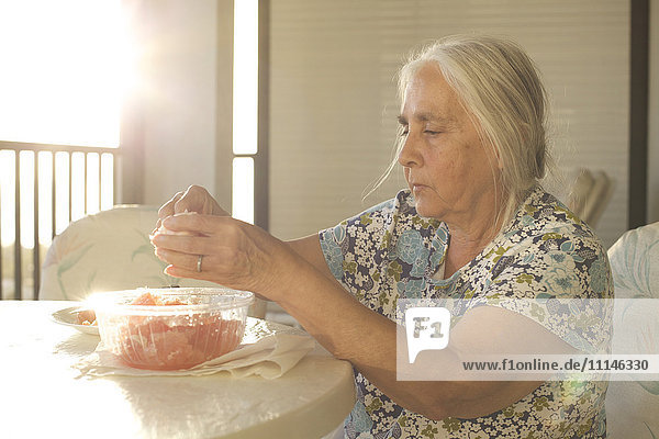Ältere Frau schält Obst am Tisch