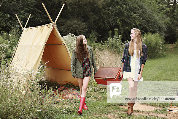 Women carrying vintage cooler near camping tent in forest