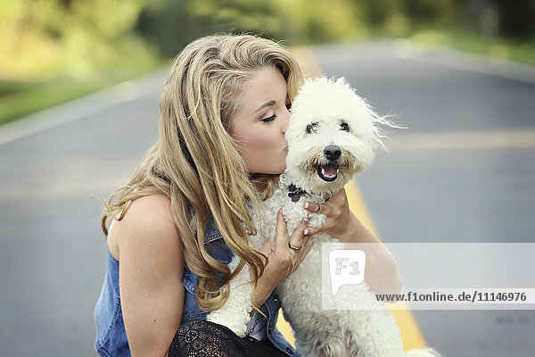 Nahaufnahme einer Frau  die einen Hund auf einer leeren Straße küsst