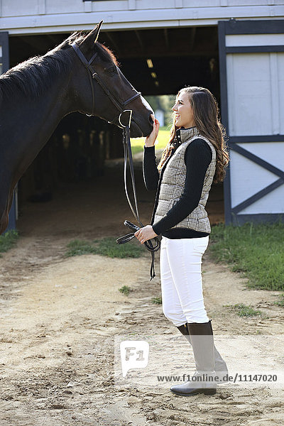 Equestrian woman petting horse at stable
