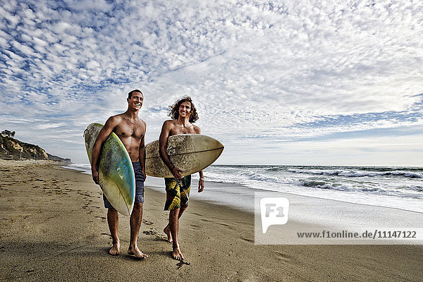 Caucasian men carrying surfboards on beach
