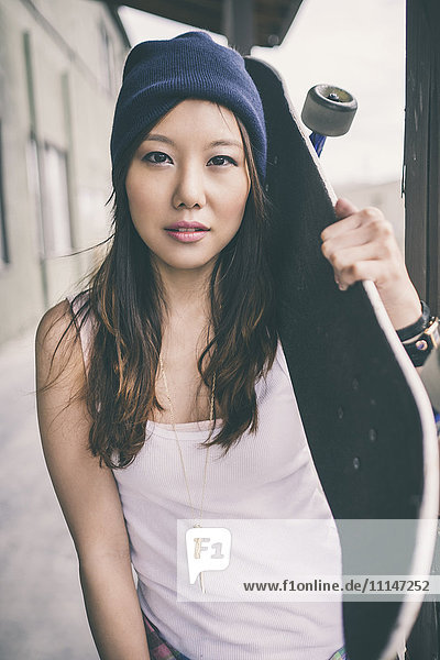 Korean woman carrying skateboard on city street