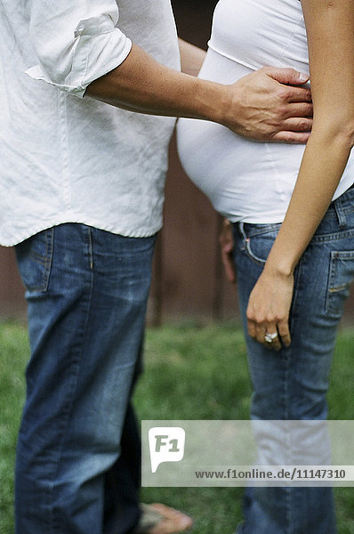 Nahaufnahme eines Mannes  der seine schwangere Frau im Hinterhof umarmt