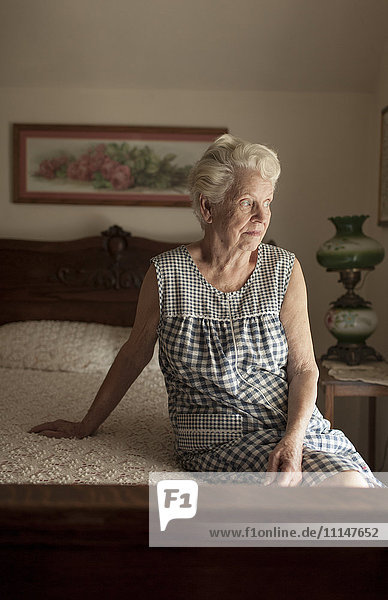 Nachdenkliche ältere Frau auf dem Bett sitzend