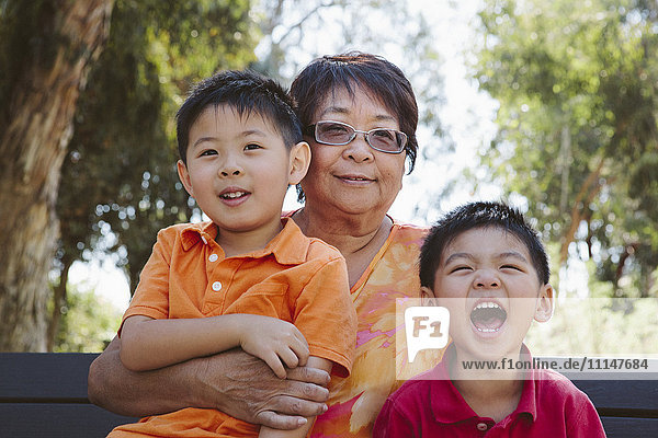Asiatische Großmutter sitzt mit Enkelkindern auf einer Bank
