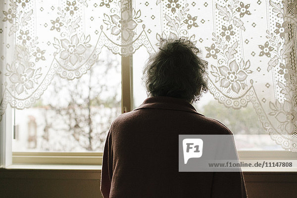Nachdenkliche gemischtrassige ältere Frau schaut aus dem Fenster