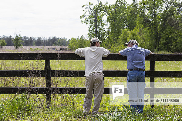 Caucasian father and son leaning on fence by rural field
