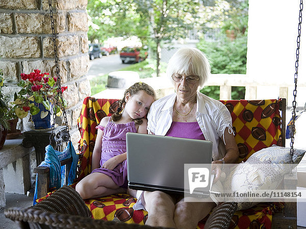 Grandmother and granddaughter using laptop on porch