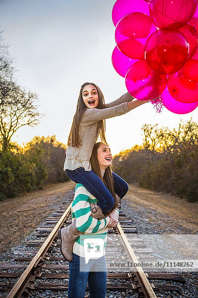 Caucasian teenage girl carrying sister on shoulders with balloons