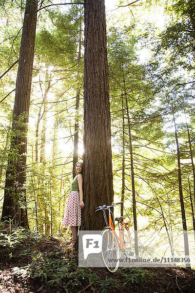Mixed race woman and bicycle in forest