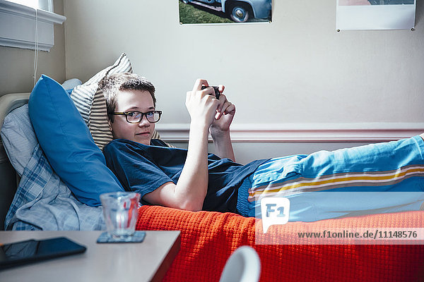 Caucasian boy using cell phone on bed