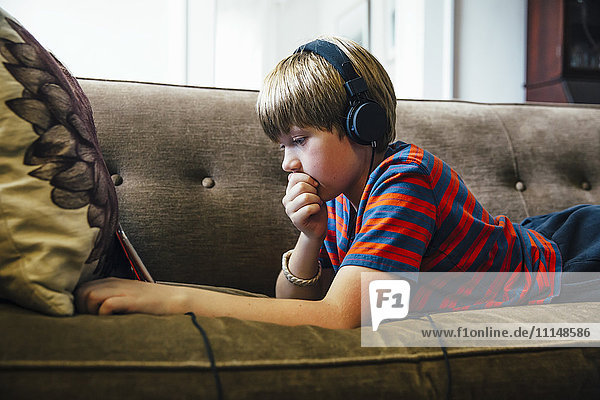 Kaukasischer Junge mit digitalem Tablet auf dem Sofa