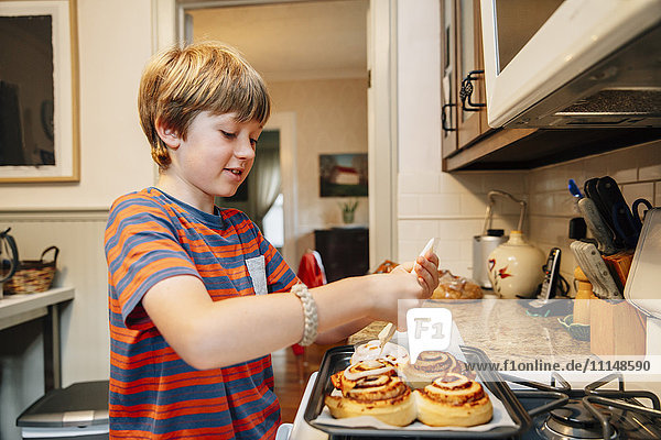 Caucasian boy frosting cinnamon rolls in kitchen