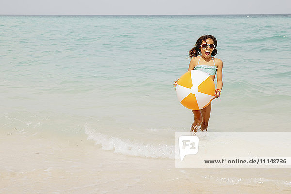 Gemischtrassiges Mädchen hält Strandball in den Wellen des Ozeans