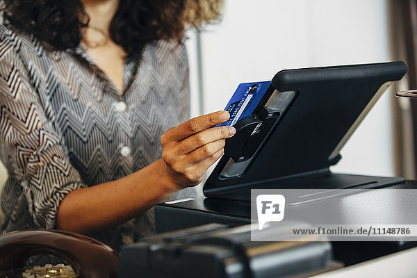 Gemischtrassiger Angestellter beim Durchziehen der Kreditkarte an der Kasse