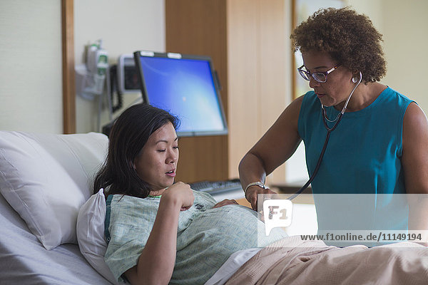 Arzt hört den Bauch einer schwangeren Patientin ab