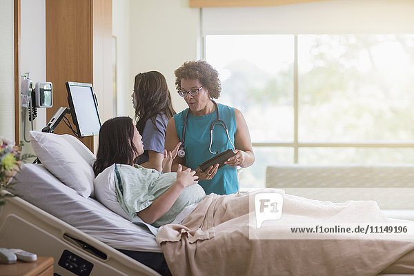 Arzt spricht mit schwangerer Patientin im Krankenhauszimmer