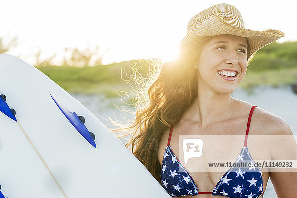 Hispanic woman carrying surfboard on beach