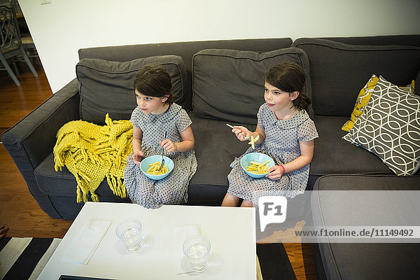 Zwillingsschwestern essen auf dem Sofa
