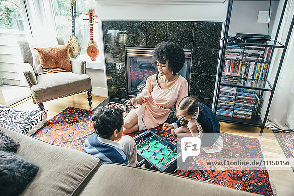 Gemischtrassige Familie spielt Tischfußball auf dem Boden des Wohnzimmers