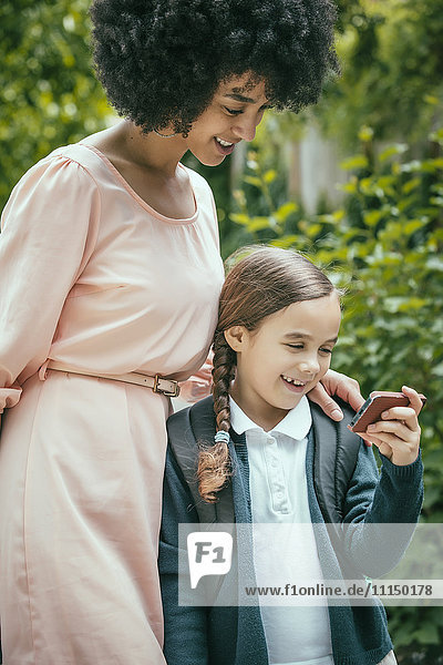 Gemischtrassige Mutter und Tochter benutzen gemeinsam ein Mobiltelefon