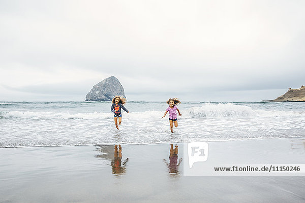 Gemischtrassige Schwestern laufen am Strand