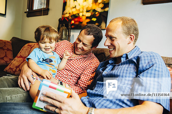 Gay fathers playing with baby son on sofa
