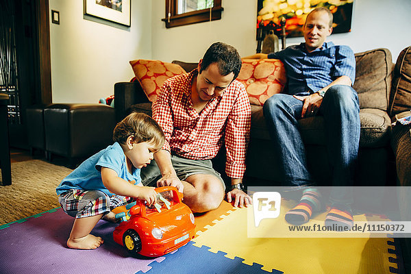 Gay fathers playing with baby son in living room