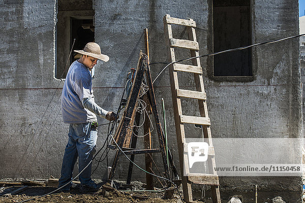 Hispanischer Arbeiter mit Drähten auf einer Baustelle