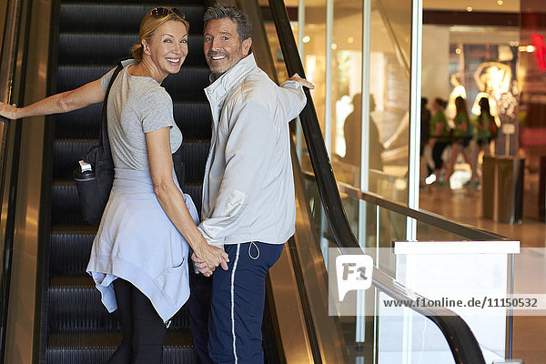 Caucasian couple riding escalator in shopping mall